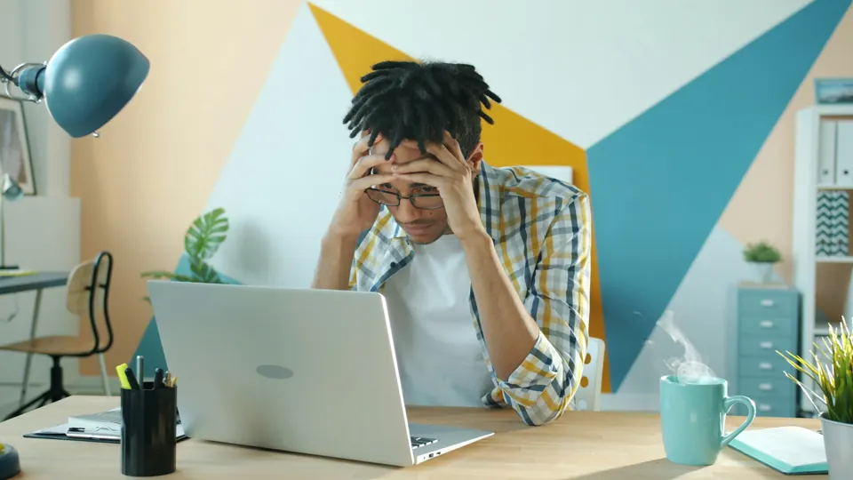 A man holding his head in frustration at his laptop